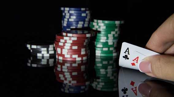 Hand holding two aces in front of stacked chips on a reflective black surface
