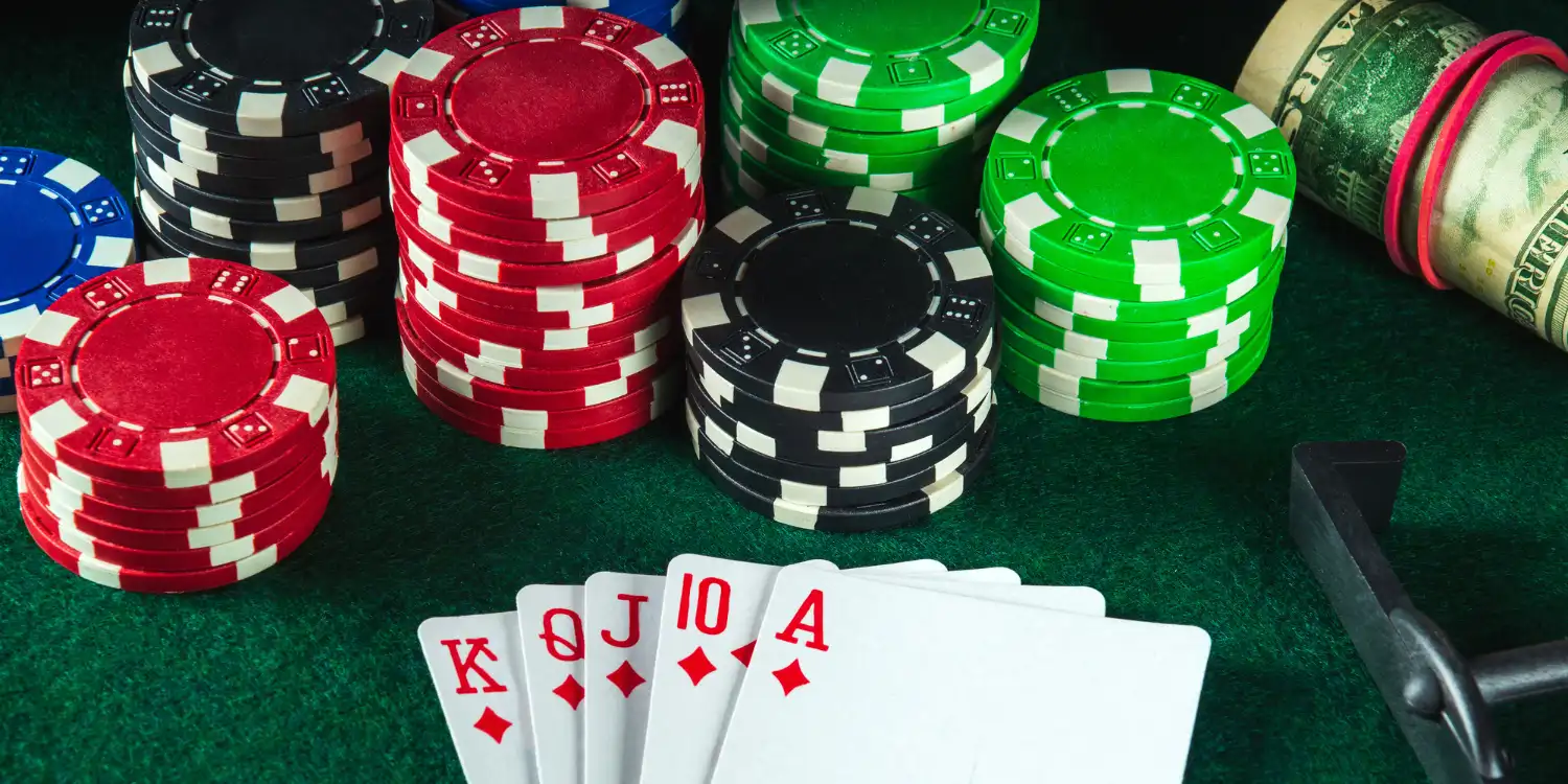 Poker chips and playing cards on a green felt table with cash rolled nearby.